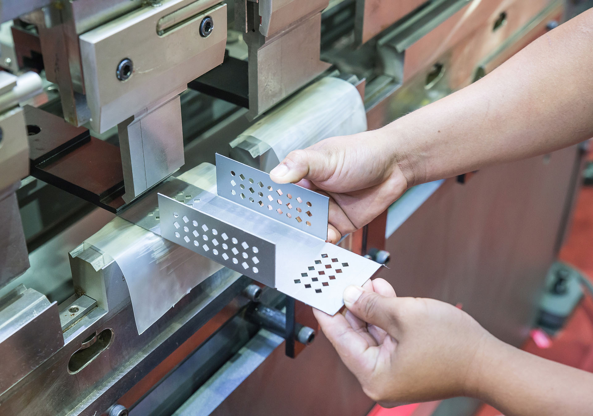 Worker handling metal sheet with perforations in industrial manufacturing process.