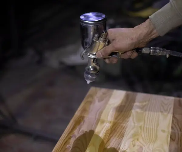 CNC routing process applying protective coating on wooden surface using spray gun for smooth finish.