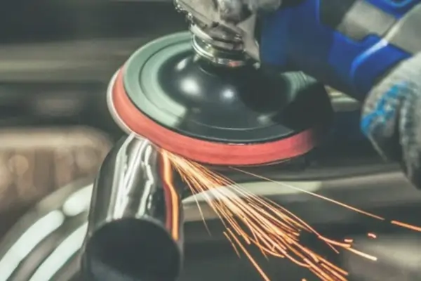 Worker creating a brushed finish on a metal tube with a power tool, generating sparks.