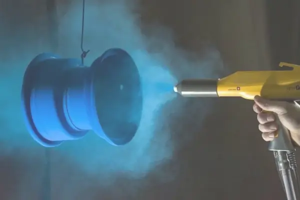 A part is being spray-painted with blue powder coating in an industrial finishing process.