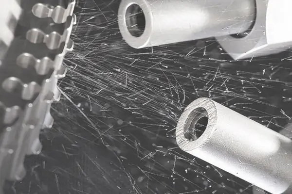 A machine bead blasting metal tubes, showing abrasive media particles flying around.