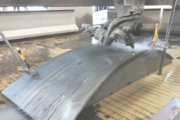 A worker using a machine to apply a brushed finish to a large, curved metal part.