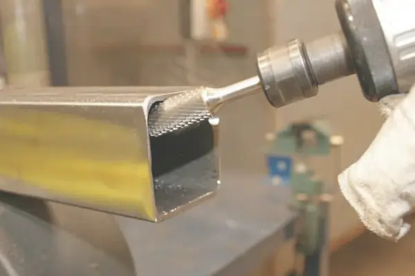 A worker deburring a metal square tube with a power tool to smooth the cut edges.
